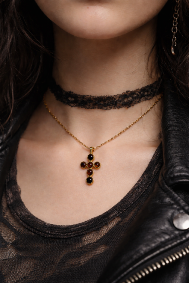 Collier doré avec croix, porté sur un haut noir avec un choker en dentelle.