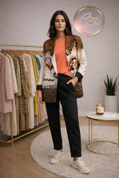 Femme en vêtement coloré avec un cardigan orné, pose devant des vêtements sur cintres.