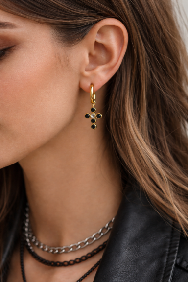 Boucles d'oreilles dorées en forme de croix avec des pierres noires accrochées.
